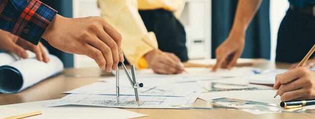 Skilled architect engineer team discuss about architectural project while project manager using laptop analysis data at meeting table with architectural document scatter around. Closeup. Delineation. - obrazy, fototapety, plakaty