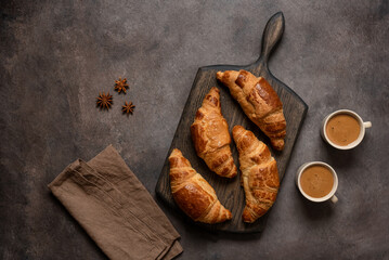 Fresh croissants and cups of coffee on a dark rustic background. Top view, flat lay. Delicious...