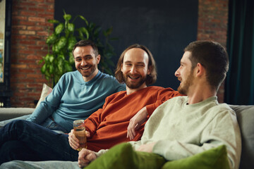 group portrait of cheerful friends watching football game, soccer match in living room on sofa and...
