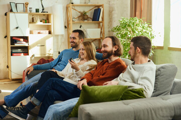 Group portrait. Guys and girl sitting on couch in living room and spending all time watching comedy...