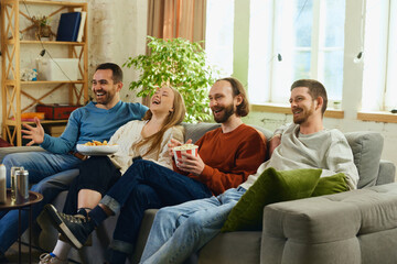 Group portrait. Guys and girl sitting on couch in living room and spending all time watching comedy...