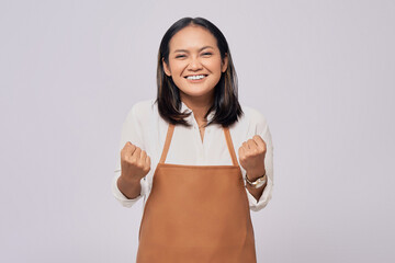 Excited young Asian woman barista barman employee wearing a brown apron working in coffee shop,...