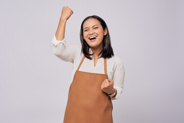 Excited young Asian woman barista barman employee wearing a brown apron working in coffee shop,...