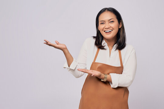 Smiling young Asian woman barista barman employee wearing brown apron working in coffee shop, pointing hand aside isolated on white background. Small business startup concept