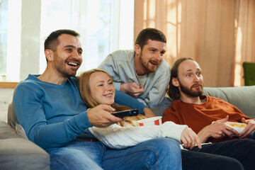 Shocked young attractive people with wide smile, laughing watching movie with comedy plot sitting on sofa in living room.