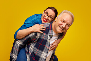 Obraz premium Smiling, beautiful happy senior woman, couple, man and woman in casual clothes posing against yellow studio background. Concept of marriage, relationship, Valentine's Day, love, emotions, fashion