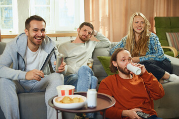 Group portrait. Guys and girl sitting in living room and spending all time watching comedy series and having fun.