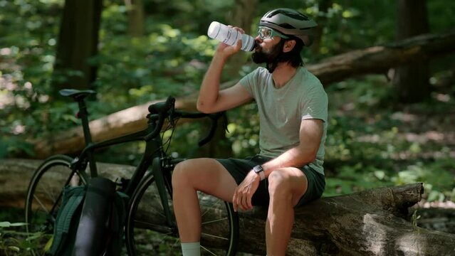 Cyclist in helmet drinks water from bottle after bike ride