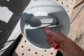 Pintor a molhar o rolo de pintor no balde que contem a tinta para aplicar na parede