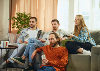 Obraz premium Group portrait of guys and girl, friends and lovely couple sitting in living room and choosing genre of movie to watch.