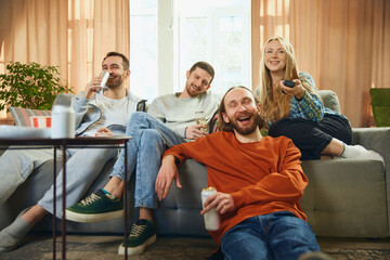 Angle view of a happy group of friends sitting on the sofa in the living room and watching a...