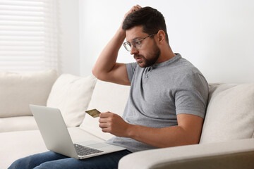 Upset man with credit card and laptop on sofa at home. Be careful - fraud
