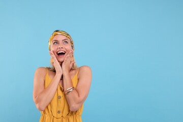 Portrait of surprised hippie woman on light blue background. Space for text