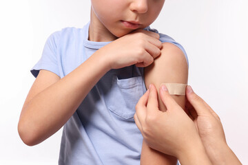 Woman sticking plaster on boy's arm after vaccination against white background, closeup