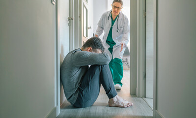 Worried female psychiatrist running to help male patient with mental disorder sitting on the floor...