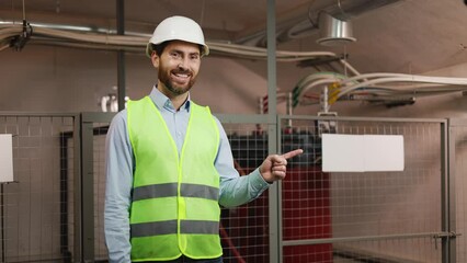 Cheerful, expert electrician gestures towards a blank signboard for advertisements at an electrical network station. The male engineer is making a hand gesture, copy space, or a template layout.