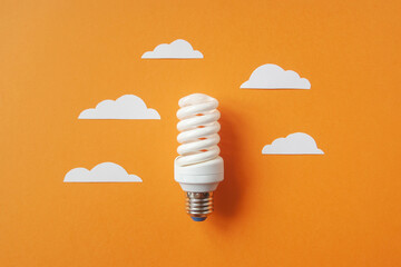 Light bulb with white cut out clouds on orange background. Idea concept. Energy and electricity. alternative energy sources. Innovation and thinking out the box symbols. Creativity and inspiration