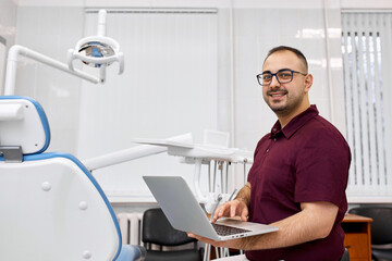 Obraz premium Professional dentist in a private office with a laptop. Online appointment booking. Healthy smile concept