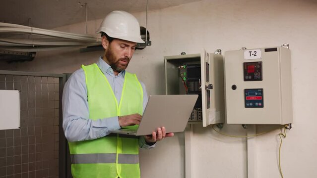 Electrical engineer man checking voltage use laptop for monitor process work at Power Distribution Cabinet in control room, preventive maintenance Yearly, professional electrician working at company.