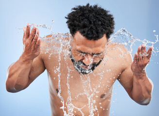 Black man, water splash and face wash for skincare, hygiene or grooming against a blue studio...