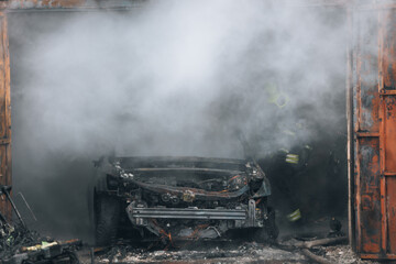 Firefighters extinguish a burning car in a garage. Burnt car. Rescuers. Strong smoke. Emergency....