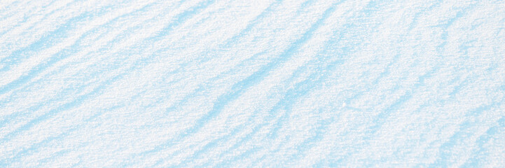 Wide panoramic winter background with snowy ground. Natural snow texture. Wind sculpted patterns on snow surface.