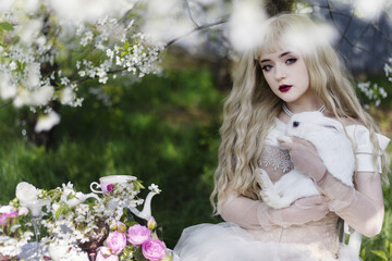 Beautiful girl with a white rabbit in a blooming apple garden. White flowers in the garden in sunlight. Spring apple trees in bloom. Beautiful girl among spring blossoms