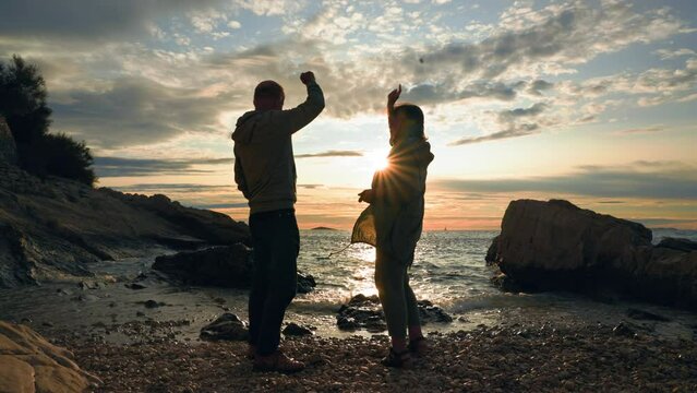 active elderly people, joyful old spouses having fun throwing stones into sea while standing on shore during summer vacation, silhouette