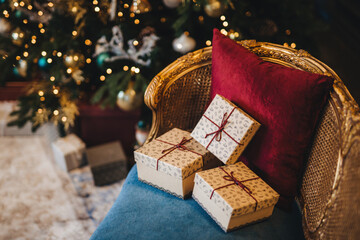 Elegant Christmas setting with wrapped gifts on a vintage chair, plush red pillow, and a beautifully lit tree.