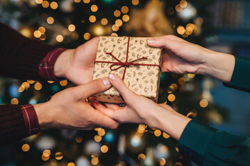 Hands exchanging a Christmas gift with care, set against a backdrop of a tree with warm golden lights