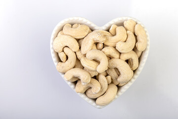 Fototapeta premium A top view of whole cashew nuts arranged beautifully in a heart-shaped bowl against a clean white background
