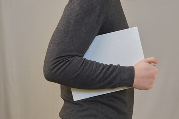 A person holds a book with a clean white cover under their arm with one hand. Preserve knowledge,...