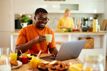 African American man using laptop while enjoying breakfast at home