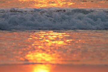 Ocean wave splashing on the beach during sunset.