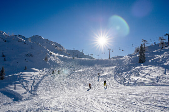 Skiers on the Vogel in Bohinj resort track on a sunny day, effect halo