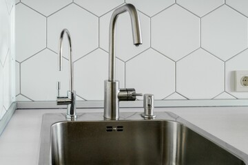 Modern kitchen, view of a metal sink with a water tap, a soap dispenser, and a faucet for purified...