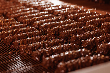 Waffles with nuts are coated with chocolate on conveyor. Production line of food factory, concept...