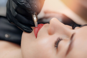 Master use tattoo machine for applying permanent makeup of red on lips woman - obrazy, fototapety, plakaty