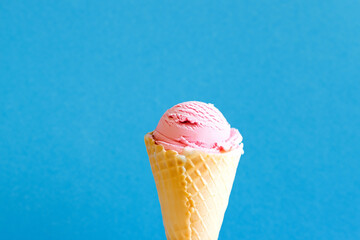 Ice cream cone with pink strawberry flavor isolated on blue background, copy space
