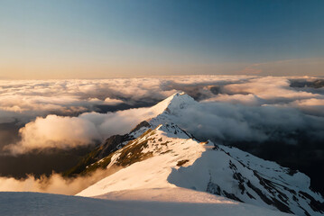 The sun sets behind a range of mountains, casting a warm glow over the clouds that envelop their...