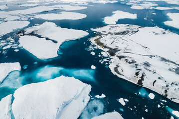 An aerial view captures the icy expanse of Antarctica, with icebergs and ice floes dotting the ocean. The scene is serene, with a sense of vastness and tranquility.