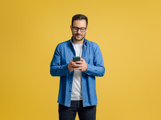 Confident serious businessman checking messages over mobile phone isolated on yellow background