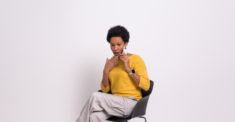 Young businesswoman with shock expression speaking on cellphone on chair against white background - obrazy, fototapety, plakaty