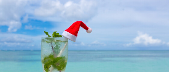 Christmas background with drinks Bocal with Santa hat on Caribbean beach.