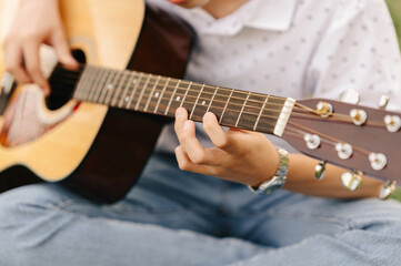 Fototapeta na wymiar Close up shot of a teen boy learning to play acoustic guitar outdoors sitting in park.