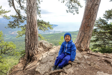 Picturesque view of the city of Yalta and the Black Sea from Ai-Petri mountain in Crimea. A boy on the background of a mountain landscape with trees in the clouds.