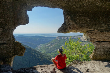 A girl inside a cave at sunset cave city Mangup-Kale, sunny day. Mountain view from the ancient...