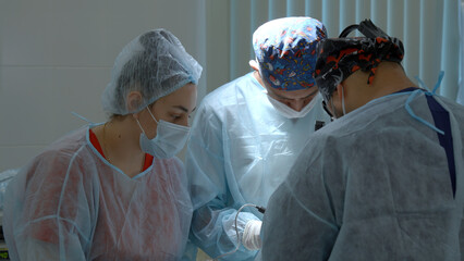 Group of surgeons working in operating room at hospital. Action. Nurse helping two doctors during...