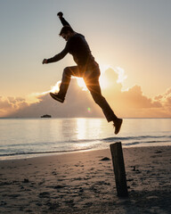 A man jumping off a post on a beach at sunset