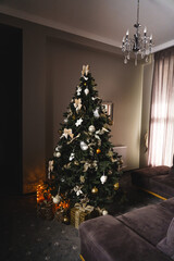 A New Year tree decorated with toys and gifts stands in the room. Christmas and New Year concept